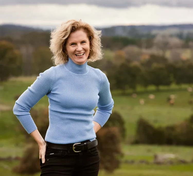Leanne smiling standing with an blurred focus view of the green farm in the background.